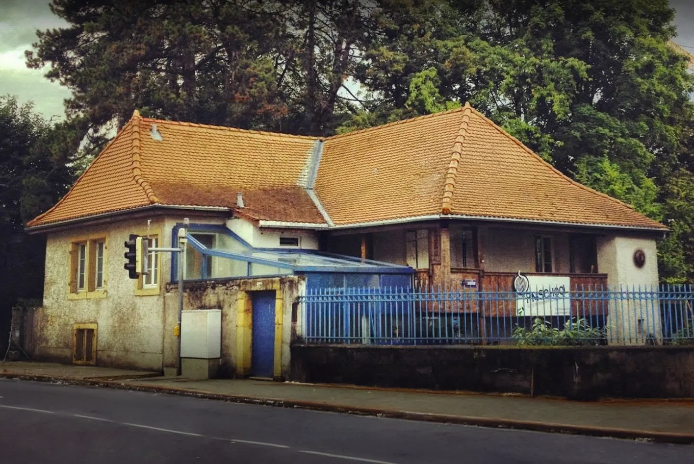 La Fodge : maison à toit de tuiles orange, véranda et barrière bleues, au bord de la route.
